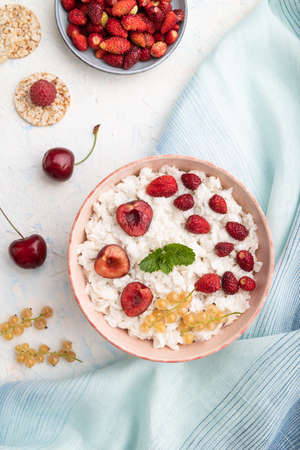 Rice flakes porridge with milk and strawberry in ceramic bowl on white concrete background and blue linen textile. Top view, flat lay, close up.の写真素材