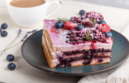 Berry cake with milk cream and blueberry jam on blue ceramic plate with cup of coffee and fresh...