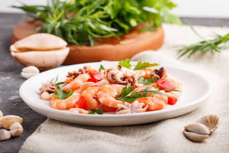 Boiled shrimps or prawns and small octopuses with herbs on white ceramic plate on a black concrete background and linen textile. side view, close up, selective focus.の写真素材