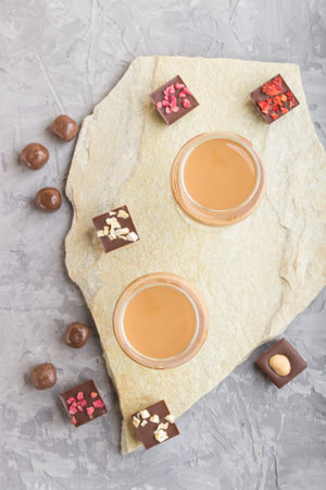 Sweet chocolate liqueur in glass with chocolate candies on a gray concrete background and stone...