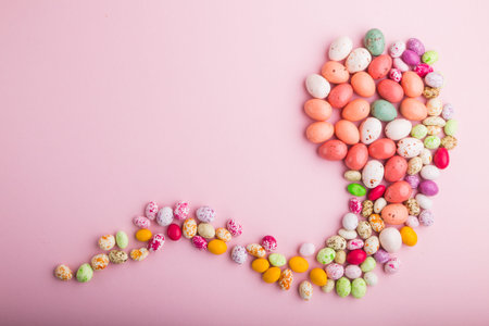 Colorful multicolored candies on a pink pastel background. Christmas cane, chocolate eggs, caramel...