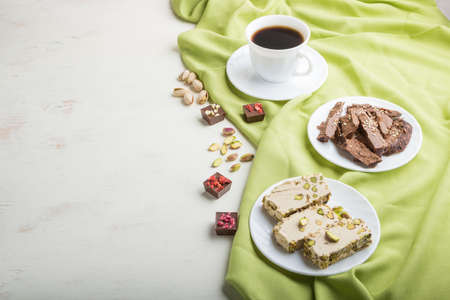 traditional arabic sweets sesame halva with chocolate and pistachio and a cup of coffee on a white wooden background and green textile. side view, copy space.の写真素材