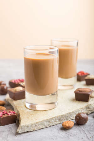 Sweet chocolate liqueur in glass with chocolate candies on a gray concrete background and stone slate board. Side view, close up, selective focus.の写真素材