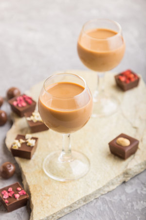 Sweet chocolate liqueur in glass with chocolate candies on a gray concrete background and stone...