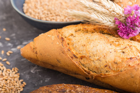 Different kinds of fresh baked bread and blue plate with grains on a black concrete background. side...