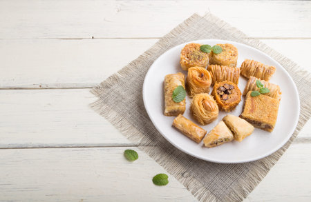 traditional arabic sweets (kunafa, baklava) on a white wooden background and linen textile. side...