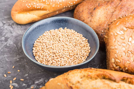 Different kinds of fresh baked bread and blue plate with grains on a black concrete background. side view, selective focus, close up.の写真素材