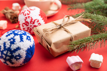 Christmas or New Year composition. Decorations, box, cinnamon, knitted balls, fir and spruce branches, cup of coffee, on a red paper background. Side view, close up, selective focus.の写真素材
