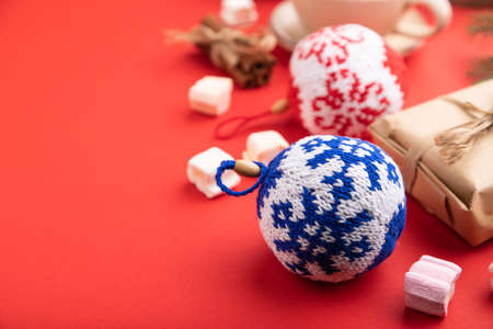 Christmas or New Year composition. Decorations, box, cinnamon, knitted balls, fir and spruce branches, cup of coffee, on a red paper background. Side view, copy space, selective focus.の写真素材