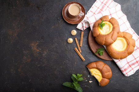 Sour cream bun with cup of coffee on a black concrete background and linen textile. top view, flat...