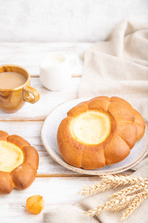 Sour cream bun with cup of coffee on a white wooden background and linen textile. Side view, close...
