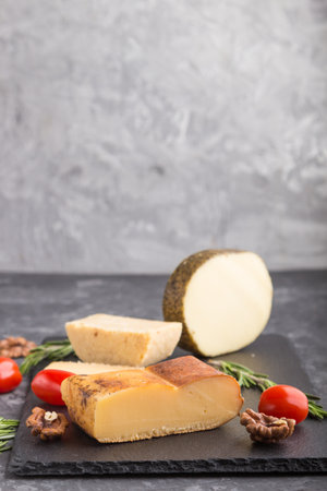 Smoked cheese and various types of cheese with rosemary and tomatoes on black slate board on a black concrete background. Side view, copy space, selective focus.の写真素材