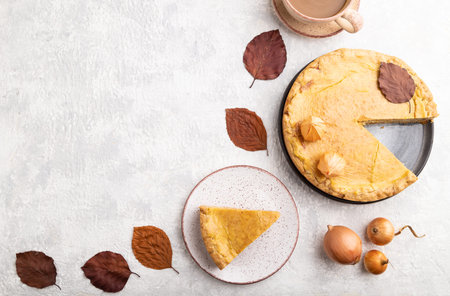 Autumn onion pie decorated with leaves and cup of coffee on gray concrete background. Top view, flat...
