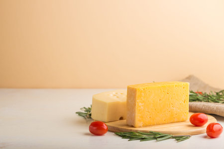 Various types of cheese with rosemary and tomatoes on wooden board on a white and orange background and linen textile. Side view, close up, copy space, selective focus.の写真素材