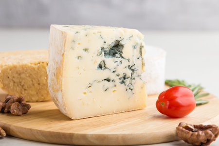 Blue cheese and various types of cheese with rosemary and tomatoes on wooden board on a white wooden...