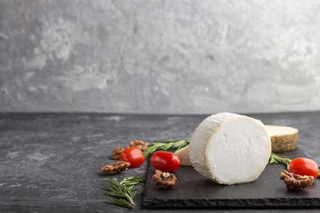 White goat cheese and various types of cheese with rosemary and tomatoes on black slate board on a black concrete background. Side view, copy space, selective focus.の写真素材