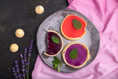 Sweet tartlets with jelly and milk cream with cup of coffee on a black concrete background and pink...