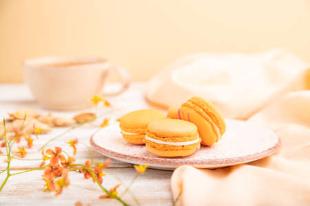 Orange macarons or macaroons cakes with cup of apricot juice on a white wooden background and orange linen textile. Side view, close up, selective focus.の写真素材