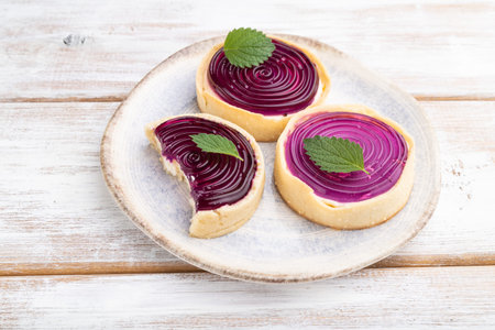 Sweet tartlets with jelly and milk cream on a white wooden background. Side view, close up.
