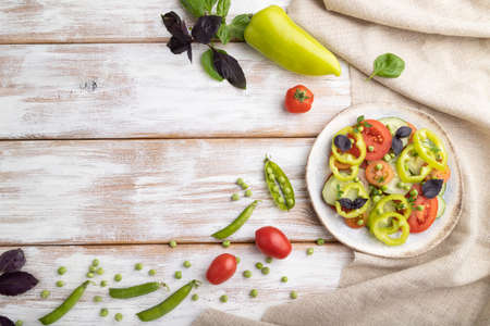 Vegetarian salad from green pea, tomatoes, pepper and basil on white wooden background and linen textile. top view, copy space, flat lay.の写真素材