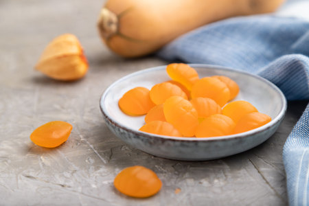 Jelly pumpkin candies on gray concrete background and blue linen textile. close up, side view, selective focus. autumn concept.の写真素材