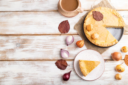 Autumn onion pie decorated with leaves and cup of coffee on white wooden background and linen...
