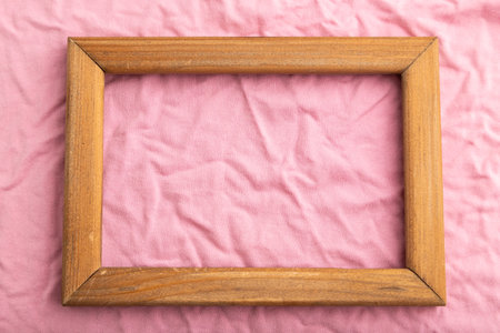Wooden frame on pink cotton tissue. Top view, flat lay, natural textile background and texture.