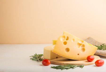 Various types of cheese with rosemary and tomatoes on wooden board on a white and orange background and linen textile. Side view, close up, copy space, selective focus.の写真素材