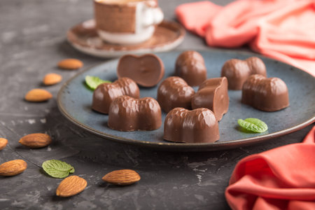 Chocolate candies with almonds and a cup of coffee on a black concrete background and red textile....