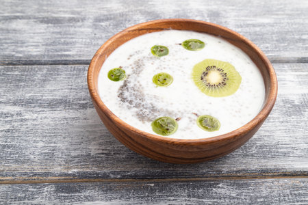 Yogurt with kiwi, gooseberry, chia and almonds in wooden bowl on gray wooden background. side view, close up.の写真素材