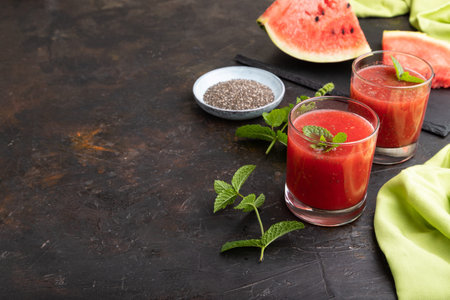 Watermelon juice with chia seeds and mint in glass on a black concrete background with green textile. Healthy drink concept. Side view, copy space.の写真素材