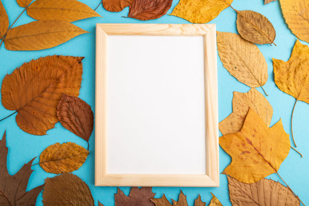 Composition with yellow and brown autumn leaves and wooden frame mockup on blue pastel background. Blank, flat lay, top view, still life, copy space.の写真素材