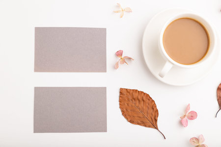 Composition with gray paper business card, brown beech autumn leaves, hydrangea flowers and cup of coffee. mockup on white background. Blank, flat lay, top view, still life, copy space.の写真素材