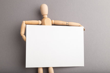 Wooden mannequin holding blank poster on gray pastel background. copy space, isolated, presentation concept.の写真素材