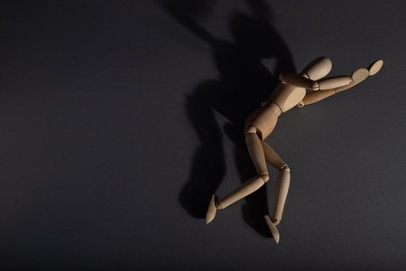 Wooden mannequin lies in a protective position on gray background. loneliness, violence, vulnerability, depression disorder concept. copy space, hard light.の写真素材