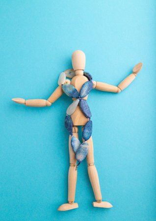 Wooden mannequin with blue agate beads on blue pastel background. copy space, isolated, luxury, bad taste, raunch, concept.の写真素材