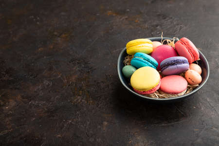 Multicolored macaroons and chocolate eggs in ceramic bowl on black concrete background. side view, copy space, still life. Breakfast, morning, concept.の写真素材