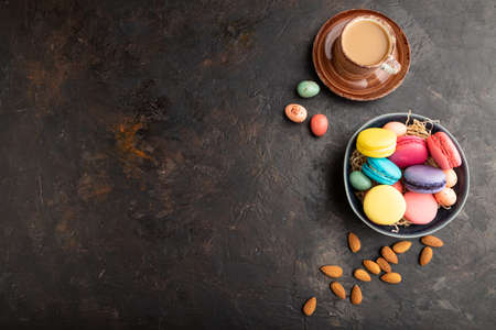 Multicolored macaroons and chocolate eggs in ceramic bowl, cup of coffee on black concrete background. top view, flat lay, copy space, still life. Breakfast, morning, concept.の写真素材