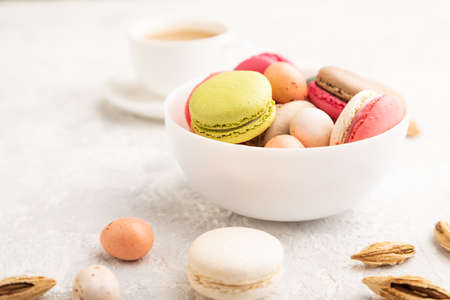 Multicolored macaroons and chocolate eggs in ceramic bowl, cup of coffee on gray concrete background. side view, close up, selective focus, still life. Breakfast, morning, concept.の写真素材