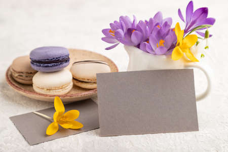 Gray paper business card mockup with spring snowdrop crocus flowers and multicolored macaroons on gray concrete background. Blank, business card, side view, copy space, still life. spring concept.の写真素材