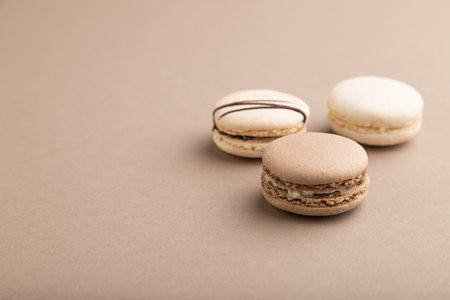 Brown and white macaroons on beige pastel background. side view, copy space, still life. Breakfast, morning, concept.の写真素材