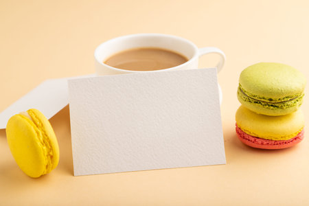 White paper business card mockup with yellow and green macaroons and cup of coffee on orange pastel background. Blank, side view, copy space, still life, close up. morning, breakfast concept.の写真素材