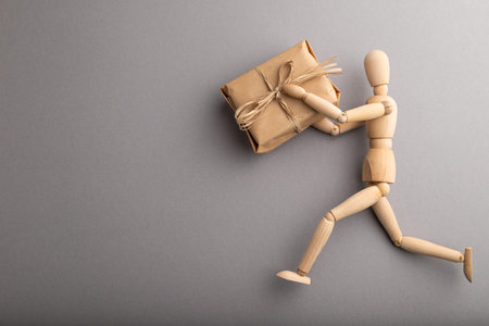 Wooden mannequin holding a gift box on gray pastel background. copy space, isolated, delivery concept.の写真素材