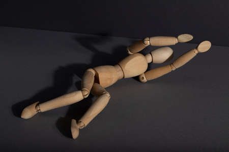 Wooden mannequin lies in a protective position on gray background. loneliness, violence, vulnerability, depression disorder concept. copy space, hard light.の写真素材