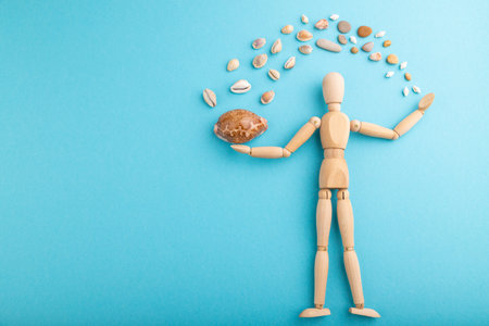 Wooden mannequin juggling sea shells on blue pastel background. copy space, isolated, travel,...
