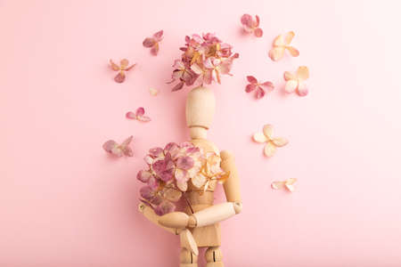 Wooden mannequin holding hydrangea flowers on pink pastel background. copy space, isolated, spring, gardening concept.の写真素材
