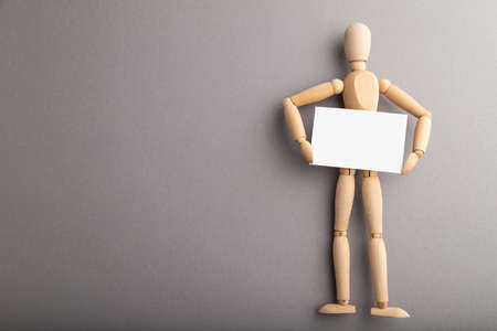 Wooden mannequin holding blank poster on gray pastel background. copy space, isolated, presentation concept.の写真素材