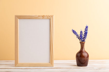 Wooden frame with blue muscari hyacinth flowers in ceramic vase on orange pastel background. side...