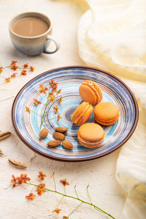 Orange macarons or macaroons cakes with cup of coffee on a white concrete background and linen textile. Side view, close up.の写真素材