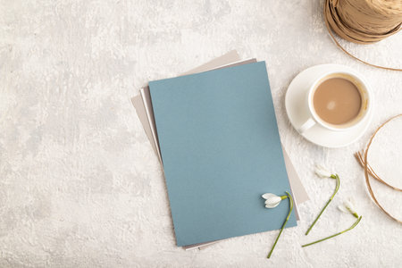 Blue paper sheet mockup with spring snowdrop galanthus flowers and cup of coffee on gray concrete...